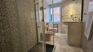 Et moderne badeværelse med brusekabine i glas, toilet og vask med spejl.