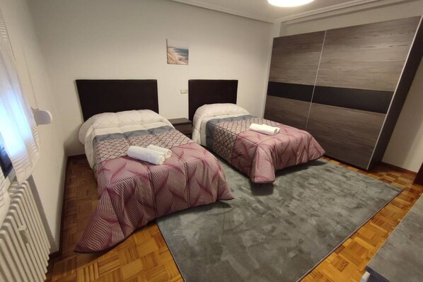 Habitación de hotel con dos camas, una alfombra gris y suelo de madera.