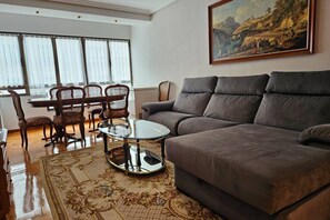 Una sala de estar con un sofá, una mesa de centro de vidrio, una mesa de comedor con sillas y un cuadro en la pared.