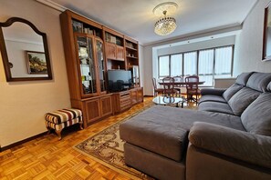 Un salon comprenant un canapé, un téléviseur, un meuble en bois, une table à manger avec des chaises et un lustre.