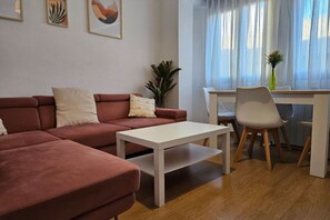 A modern living room with a sofa, a coffee table, a dining table with chairs, and a window with curtains.