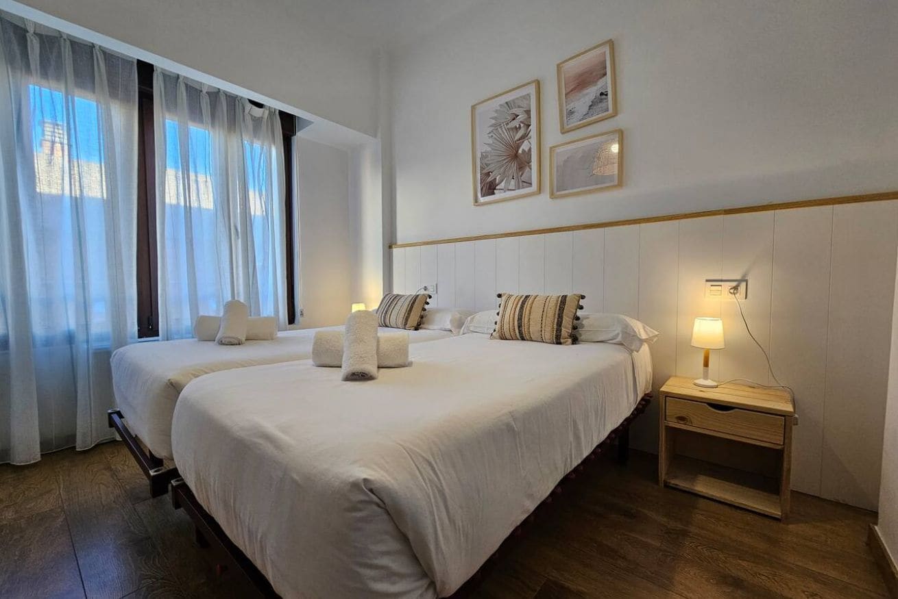 A hotel room with two beds, a nightstand, a lamp, and artwork on the wall.
