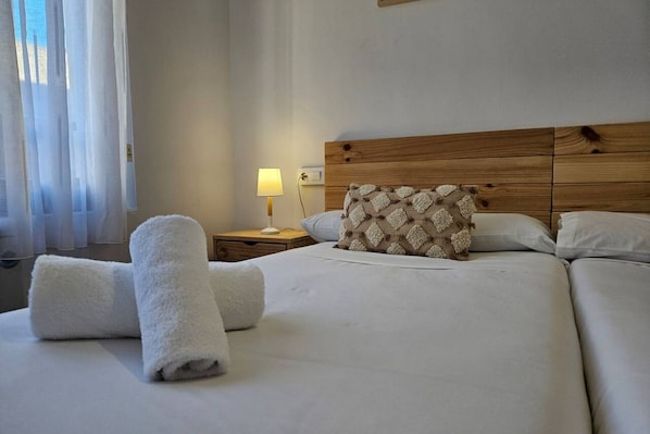A hotel room with a bed, a nightstand with a lamp, and a window with sheer curtains.
