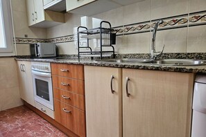 A kitchen with a microwave, oven, sink, and a dish rack.