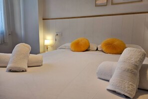 A hotel room with a neatly made bed, two pillows, a bedside lamp, and rolled towels.