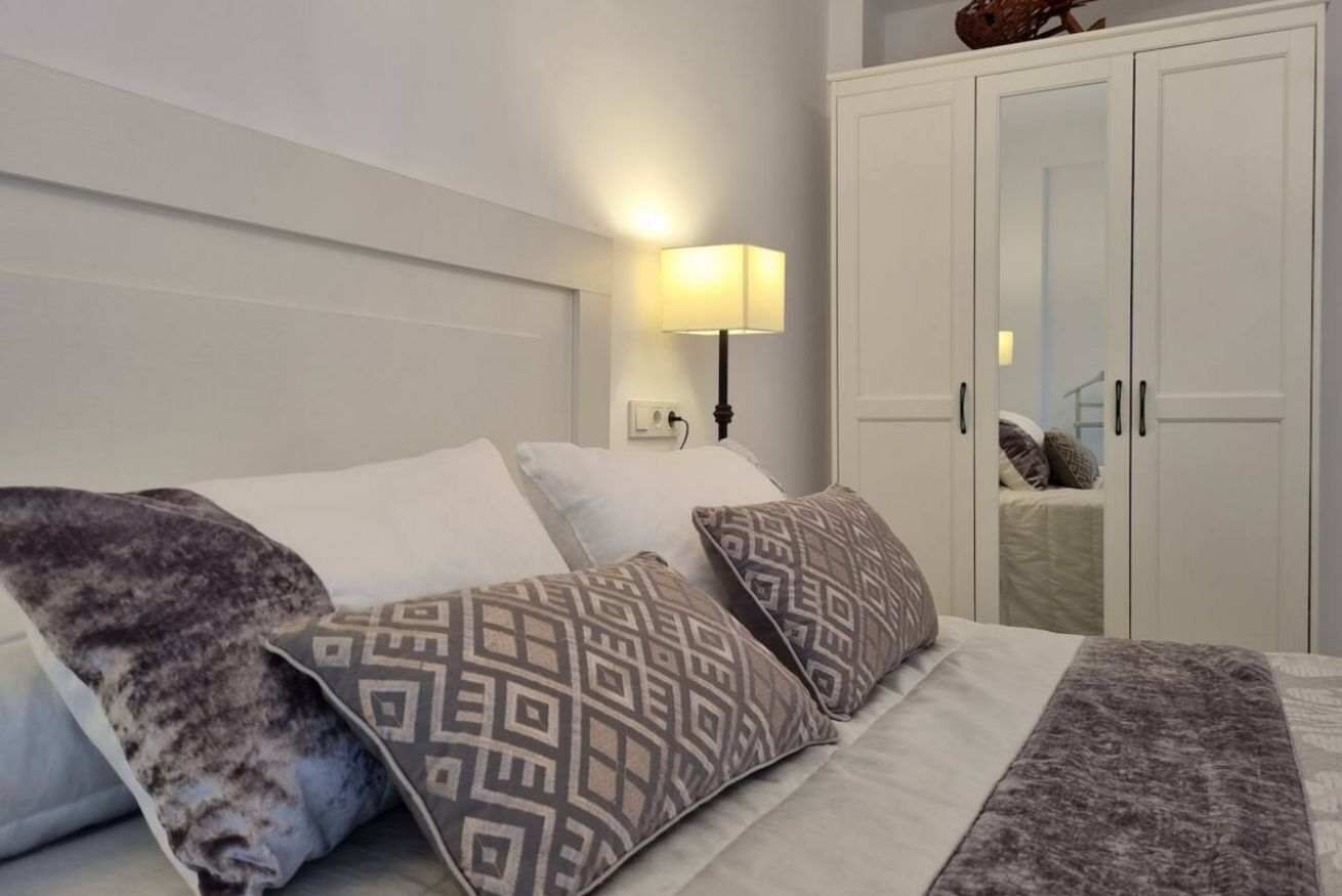 Een slaapkamer met een bed, gestreepte kussens, een bedlampje en een kledingkast.