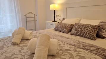 A neatly made bed with patterned pillows, a bedside lamp, and rolled towels on a patterned bedspread.