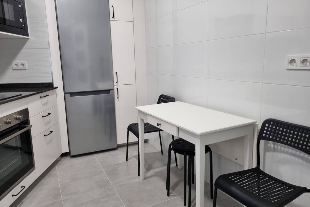 Een functionele keuken met een koelkast, oven en een eettafel met twee stoelen.