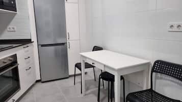 A compact kitchen with a refrigerator, oven, and a small dining table with two chairs.
