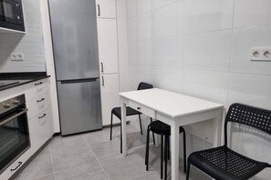 A compact kitchen with a refrigerator, oven, and a small dining table with two chairs.