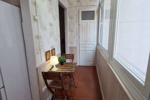 Ein schmaler Korridor mit einem Holztisch, Stühlen, einer weißen Tür und einem Fenster zur rechten Seite.