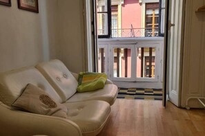 Ein beiges Sofa mit einem gemusterten Kissen, einer grün-gelben Decke und einer karierten Fußmatte.