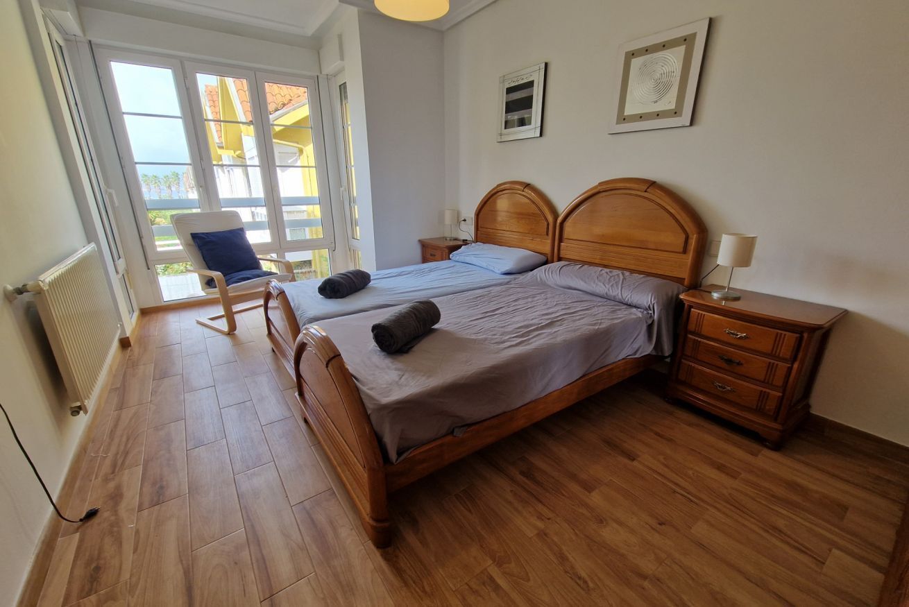 A double bed with wooden headboard, a nightstand, a chair, and a view of the outside.