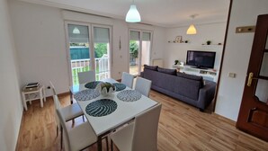 Een woonkamer met een bank, televisie en een eethoek met een tafel en stoelen.