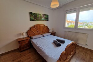 Un dormitorio con cama de madera, una mesita de noche, una lámpara, un cuadro de una cascada y una ventana con vistas.