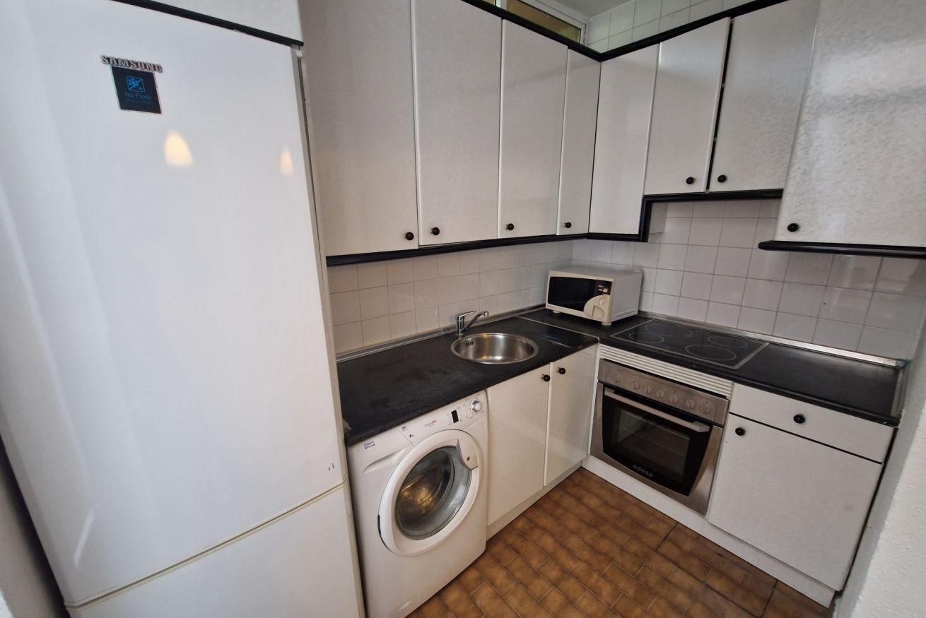 A compact kitchen with white cabinets, a washing machine, a microwave, and a stove.