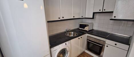 A compact kitchen with white cabinets, a washing machine, a microwave, and a stove.