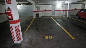 A parking garage with marked parking spaces, a fire extinguisher, and a red car parked in one of the spaces.