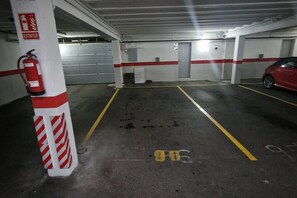 A parking garage with marked parking spaces, a fire extinguisher, and a red car parked in one of the spaces. - 158A Rinconin Triplex with Pool (Gijón)