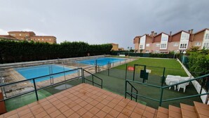 A swimming pool area with a green deck, a fenced pool, and a staircase leading to a terrace.