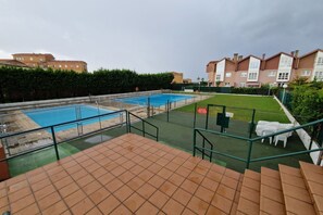 A swimming pool area with a green deck, a fenced pool, and a staircase leading to a terrace.