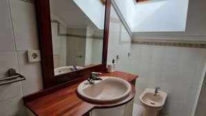 A bathroom with a wooden vanity, a sink, a bidet, a mirror, and a skylight.