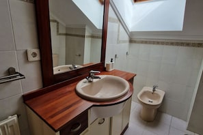 A bathroom with a wooden vanity, a sink, a bidet, a mirror, and a skylight.