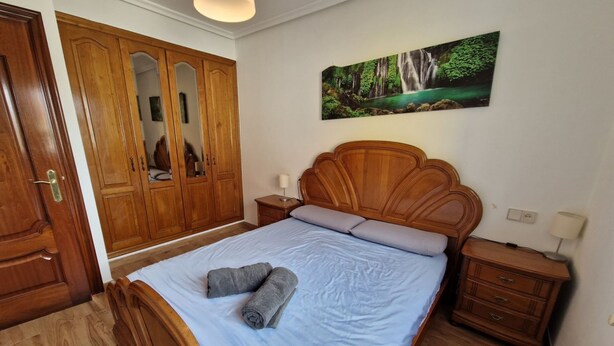 A bedroom with a bed, wooden wardrobe, nightstands, and a painting of a waterfall.