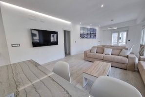 Un salon moderne avec un téléviseur à écran plat, un canapé beige, une table basse en bois et une table à manger en marbre.
