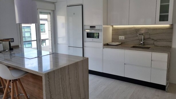A modern kitchen with white cabinetry, a marble countertop, and a built-in oven.