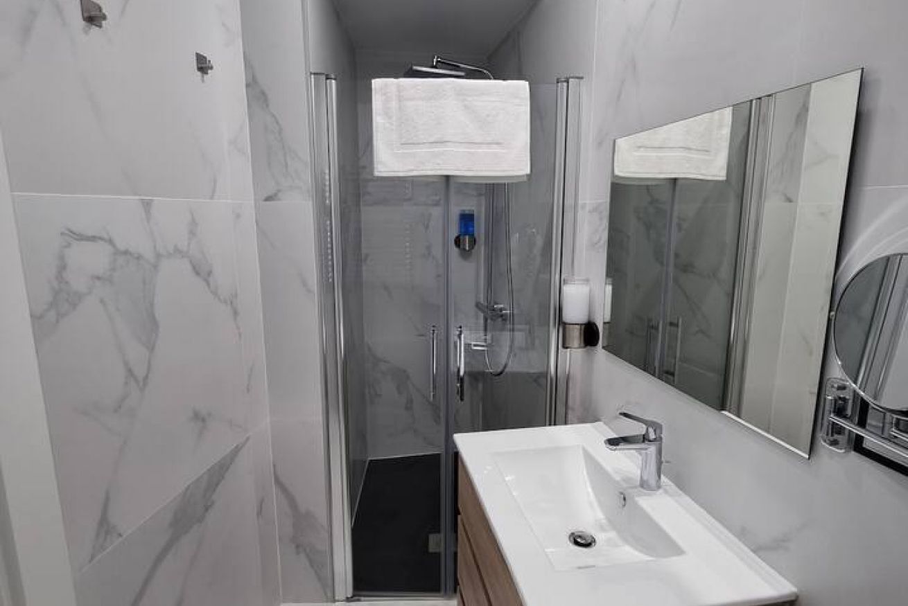 Un baño moderno con cabina de ducha de vidrio, un lavabo blanco y un espejo grande.