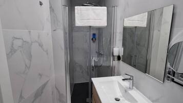 Un baño moderno con cabina de ducha de vidrio, un lavabo blanco y un espejo grande.