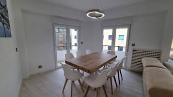 A modern dining area with a wooden table and white chairs, large windows, and a beige sofa.