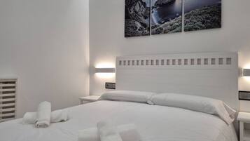 Habitación de hotel con una cama grande, ropa de cama blanca, cabecera blanca y una obra de arte colgada en la pared que representa una escena costera.