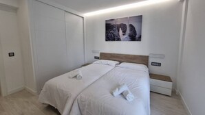 Un lit double avec du linge de lit blanc, une tête de lit, des tables de chevet et une œuvre d’art accrochée au mur.