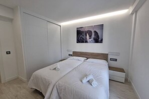 Un lit double avec du linge de lit blanc, une tête de lit, des tables de chevet et une œuvre d’art accrochée au mur.
