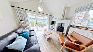 A modern living room with a sofa, a coffee table, a fireplace, and a TV. - Stunning Beach House - Sleeping 4 in 2 Bedrooms - Pool and Beach Access Included. (Primrose Valley)