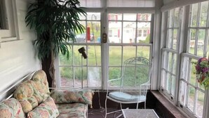 A conservatory with a cushioned bench, a small table, and a potted plant. - The Red Mill House (Goldsboro)