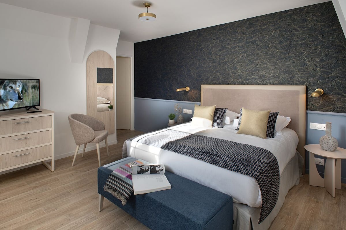 A modern bedroom with a large bed, a TV, a desk, and a chair.