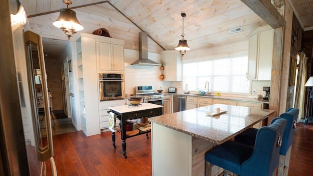 A spacious kitchen with wooden floors, white cabinets, a central island with bar stools, and pendant lighting. - High Point Retreat in the Heart of Mentone! (Mentone)