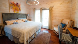 A cozy bedroom with a large bed, a wooden headboard, a chandelier, a window with curtains, and a houndstooth patterned chair. - High Point Retreat in the Heart of Mentone! (Mentone)