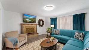 Una sala de estar con sofá, sillón, chimenea y un cuadro en la pared.