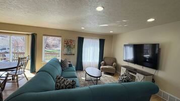 Una sala de estar con sofá, sillones, una mesa de centro, televisor y un comedor con sillas y una mesa.