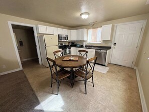 A kitchen with white cabinets, a round dining table with chairs, a refrigerator, a microwave, and a dishwasher.