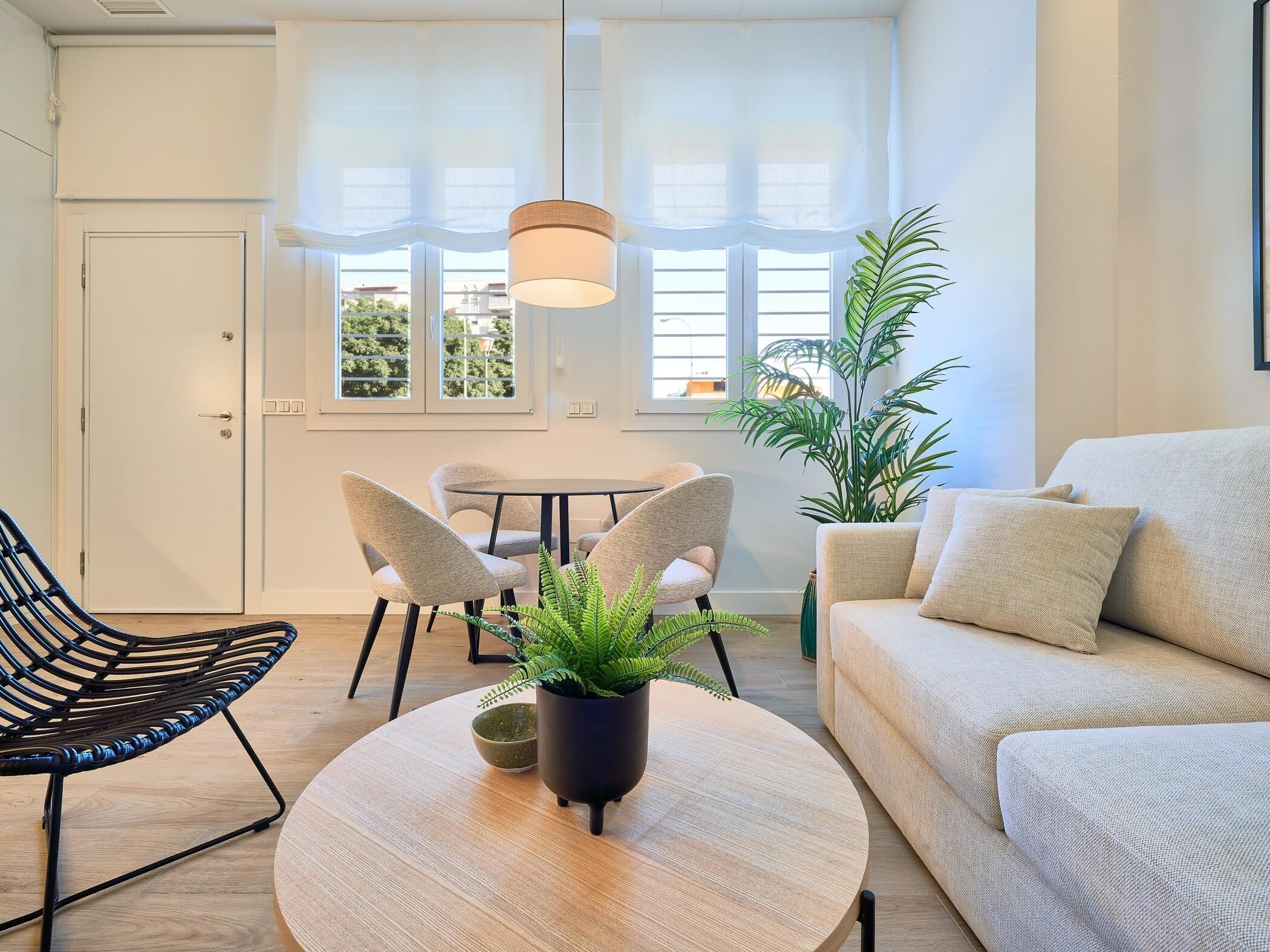 Una sala de estar moderna con una mesa redonda de madera, dos sillas, un sofá y una planta en maceta.