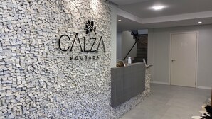 A reception area with a stone wall, a reception desk, and a staircase leading to an upper floor. - Pousada Calza (Bento Goncalves)