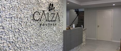 Zona de recepción con pared de piedra, mostrador de recepción y escalera que sube a un piso superior.