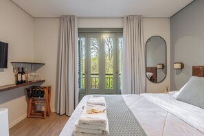 A hotel room with a bed, a wooden chair, a shelf with bottles and glasses, a mirror, and a view of greenery through the door. - Pousada Calza (Bento Goncalves)