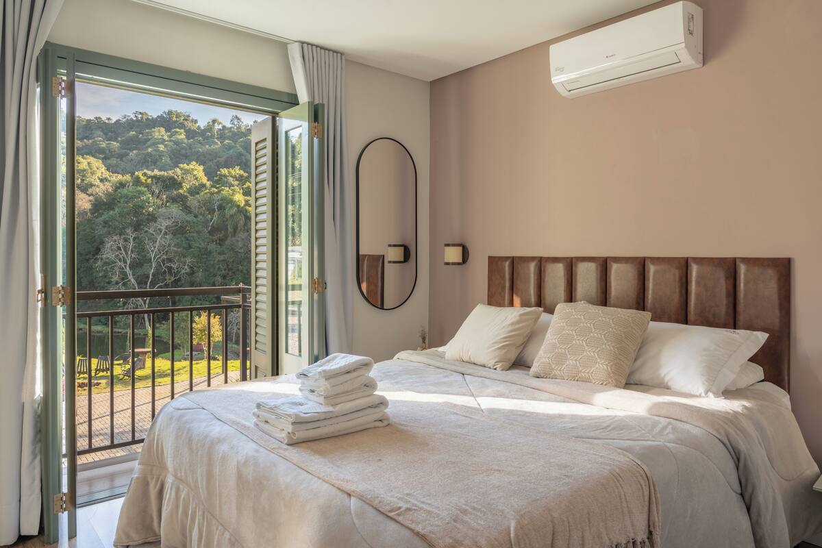 Un dormitorio con cama, espejo, equipo de aire acondicionado y vista a un jardín.