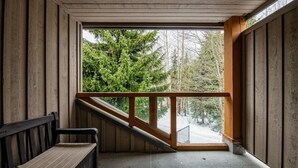 A wooden cabin with a bench and a wooden railing overlooking a snowy landscape with trees.